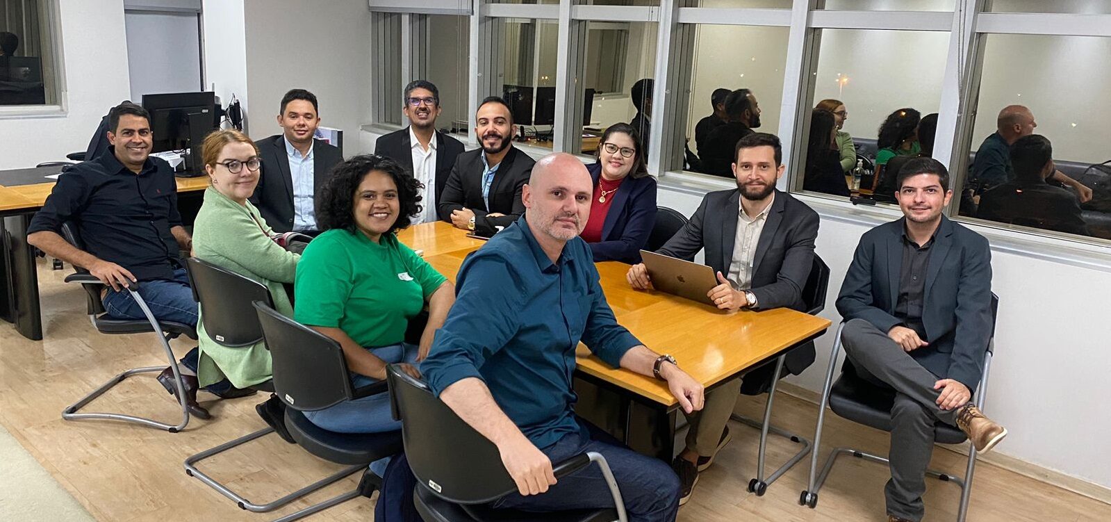 Representantes do NEES sentados ao redor de uma mesa retangular amarela, todos olham para a foto